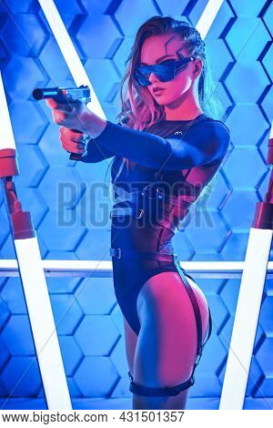 Cyber world of the future. Attractive sci-fi cyber warrior girl in black bodysuit and protective glasses stands on alert with a gun among neon lamps. Game, virtual reality.