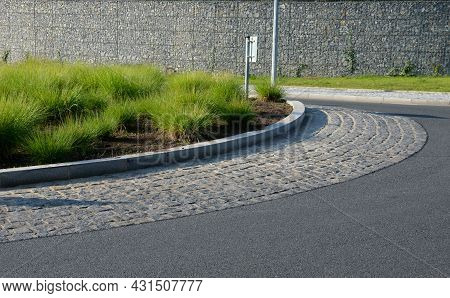 Roundabout Of Gray Granite Cubes Closer To The Center. Beveled Concrete Curbs With Flowers And Grass