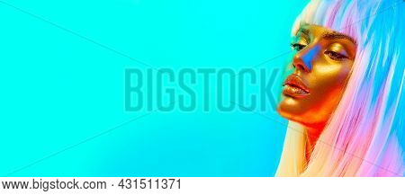 Fashion model woman face in bright neon colourful lights, beautiful sexy girl with white hair and trendy glowing gold skin make-up. Art design make up. Glittering, golden, metallic shine makeup