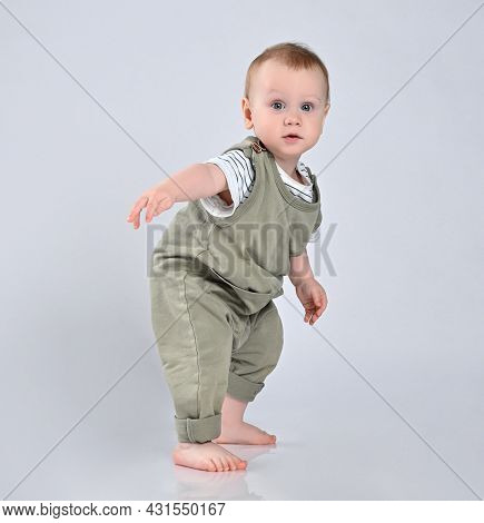 Small Child Tries To Walk For A Year, Balances. Hes Wearing A Green Cotton Jumpsuit And A Light T-sh