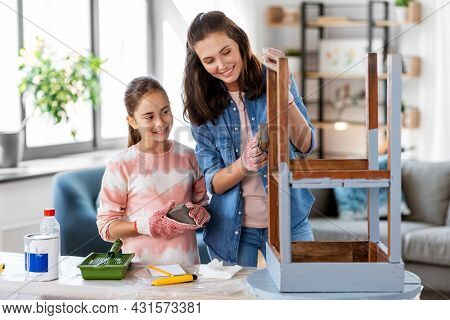 furniture renovation, diy and home improvement concept - happy smiling mother and daughter sanding old round wooden table with sponge at home