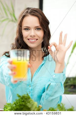 femme tenant le verre de jus d'orange et de montrer signe ok