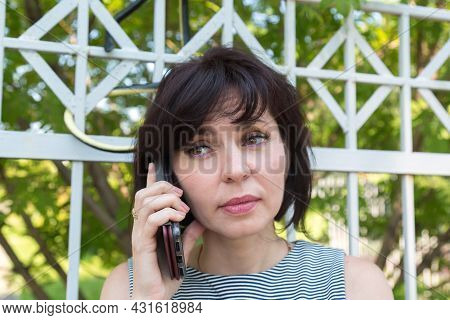 A Woman Is Talking On The Phone On The Street By Fence Not Noticing A Poisonous Snake Near Her Head.