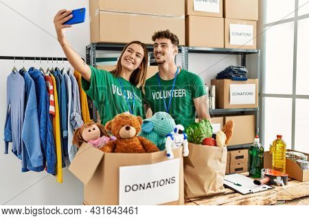 Young hispanic volunteer couple smiling happy make selfie by the smartphone at charity center.