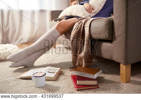 people and leisure concept - young woman in knee socks with books and drink in mug on floor sitting on sofa at home