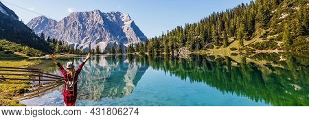 Female Traveller In Warm Clothes From Back, Standing At Mountain Lake Coast Enjoying The View Of The