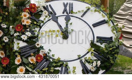Large Wall Clock On The Field In Blooming Flowers, Showing The Time 11:55, 12:00. Time Management Co