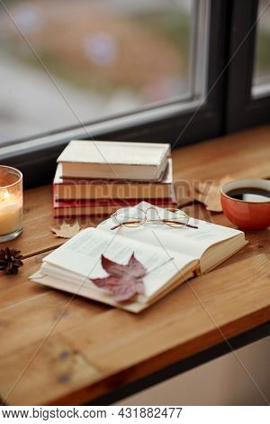 season, leisure and objects concept - open book, cup of coffee, autumn leaves and candle on window sill at home