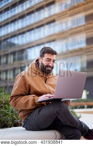 Vertical Photo Of A Man Using Laptop Outdoors. Businessman With A Nice Smile Works Remotely On The S