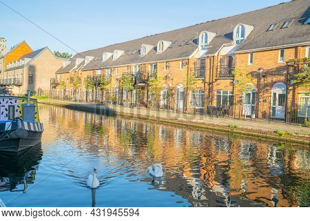Canal-side Apartments Reflected In Calm Water In Morning Light With Two White Swan On Shady Side Of 