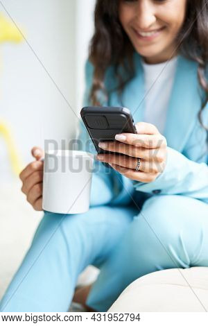 Close-up Of Unrecognizable Business Womans Hands Holding A Cup Of Coffee Sitting On A Sofa While Usi