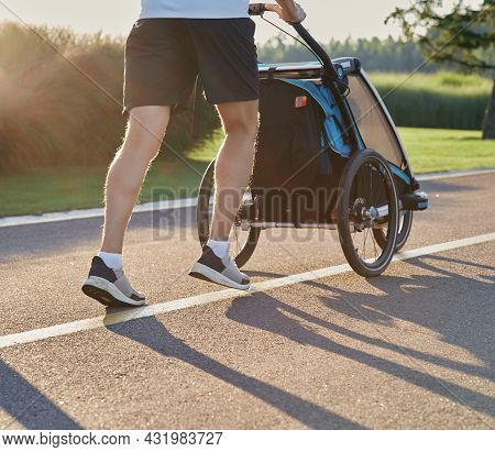 Running Man With Baby Jogging Stroller In Motion Enjoying Workout And Summer Day In City Park. Back 
