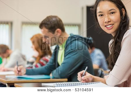 Portrait of a smiling female student with others writing notes in the classroom