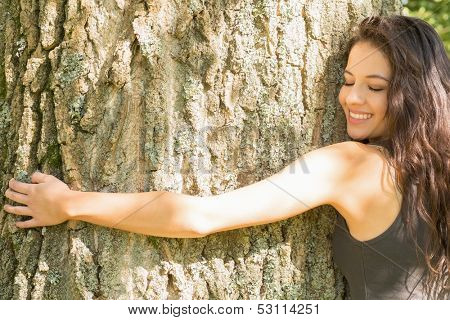Casual happy brunette embracing a tree with closed eyes in a park on a sunny day
