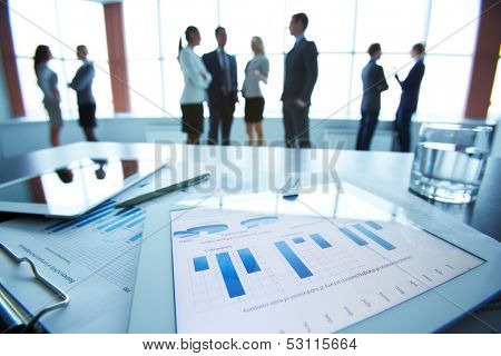 Close-up of business document in touchpad lying on the desk, office workers interacting in the background