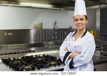 Young smiling chef standing arms crossed in front of hotplate in professional kitchen