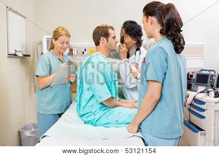 Doctor with ophthalmoscope examining patient's eye while nurses standing by in hospital