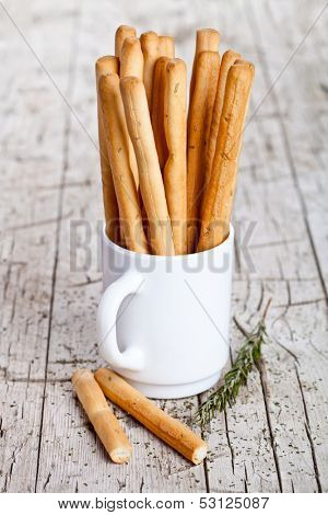 cup with bread sticks grissini and rosemary on rustic wooden background