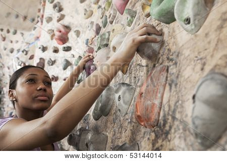 Determined young woman climbing up climbing wall 