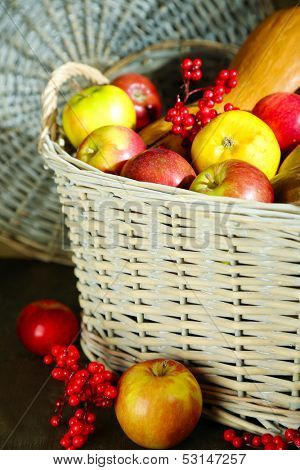 Juicy apples and pumpkin in wooden basket on table close-up