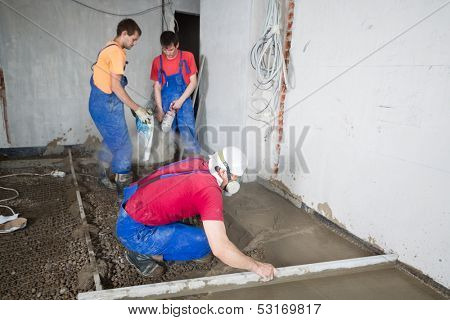 Three workers poured concrete floor in construction room
