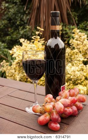 Bottiglia e bicchiere di vino rosso con uva sul tavolo patio