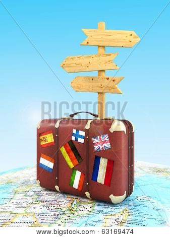 wood sign board and old suitcase with striples flags on blurred world map and sky in background