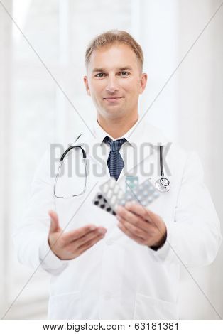 healthcare, medical and pharmacy concept - young male doctor with packs of pills