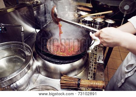 Chef is stirring vegetables with sour sauce in wok, toned