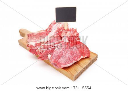 Studio shot of raw beefsteaks on a cutting board with a price tag isolated on white background