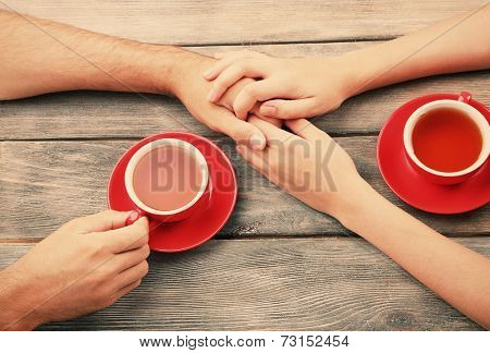 Tea cups and holding hands at the wooden table