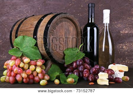 Wine in bottles, Camembert and brie cheese, grapes and wooden barrel on wooden table on wooden background