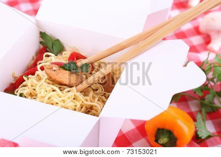 Chinese noodles and sticks in takeaway box on fabric background