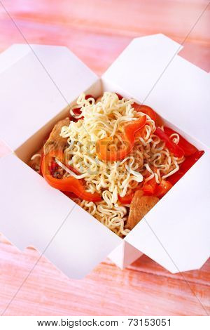 Chinese noodles with meat and pepper in takeaway box on pink background