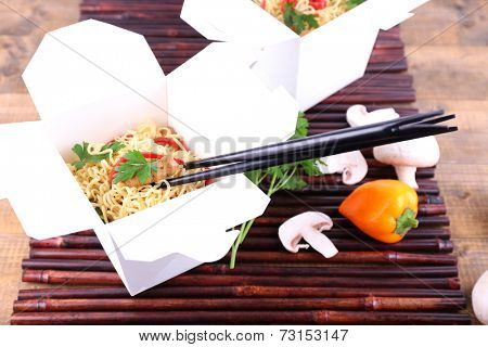 Chinese noodles in takeaway boxes on bamboo mat on wooden background
