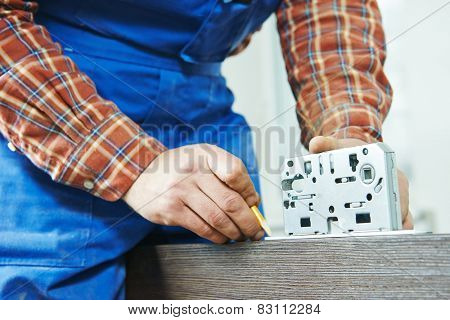 Close-up carpenter hands with doorlock during lock process installation into wood door