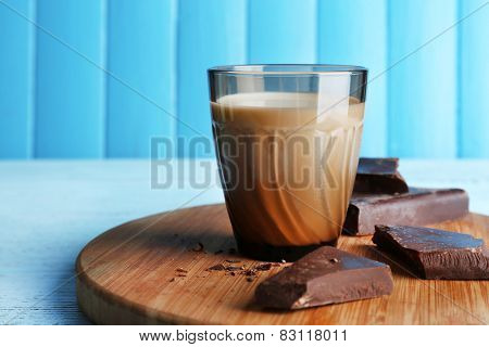 Glass of milk with chocolate chunks on cutting board and color wooden planks background