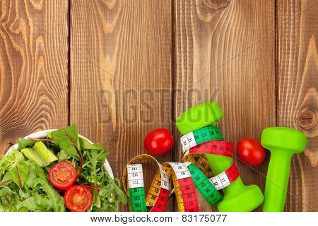 Dumbells, tape measure and healthy food over wooden table with copy space. Fitness and health