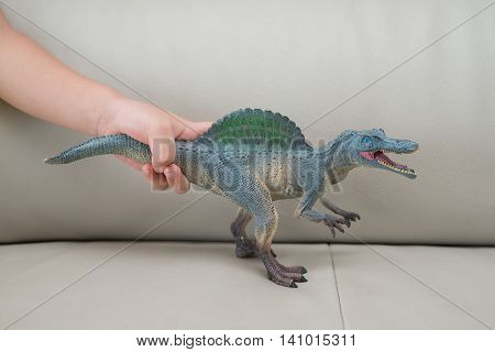 kids hand catching a greu spinosaurus toy on a sofa at home