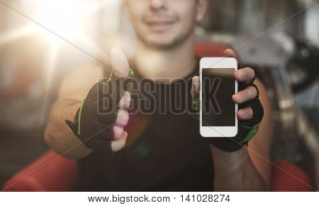 sport, bodybuilding, lifestyle, technology and people concept - happy young man with smartphone showing thumbs up in gym