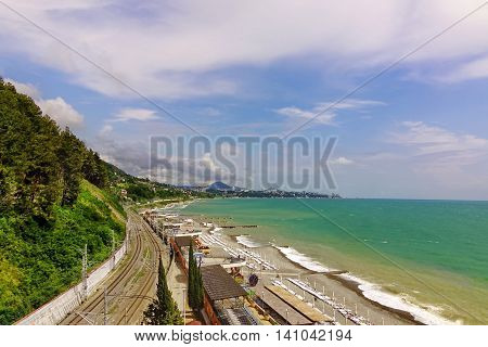 Russian Railway Track Running Along The Black Sea Shore Beach. Horizontal Summer Landscape. The view from Dagomys Village In The Direction To Sochi City. Internal Travel Concept.