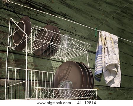Clean washed dish ware drying on a drainer mounted on the wooden wall angled filtered outdoor shot