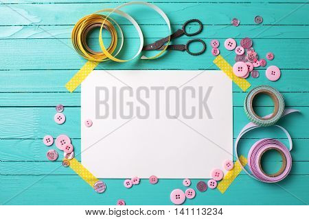 Sewing thread - buttons scissors ribbon and empty tag on turquoise wooden background. Selective focus. Scrapbboking. Flat lay. Place for text.