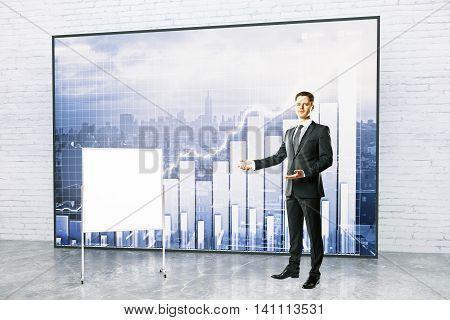 Handsome young businessman giving presentation with blank flipboard and forex chart on city background. Mock up