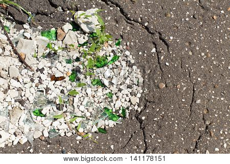 A hole in an old paved footpath covered with white stone (gravel) and broken glass.