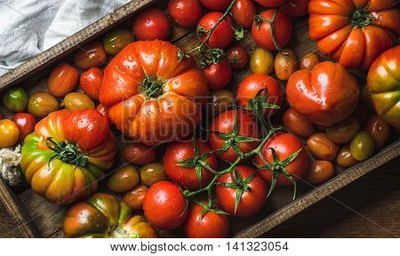 Colorful tomatoes of different sizes and kinds in dark wooden tray, top view, horizontal composition