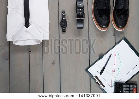 Businessman work outfit on grey wooden background. White shirt with black tie watch belt oxford shoes planchette and calculator. Back to work. Copy space frame. Set of mans fashion and accessories.