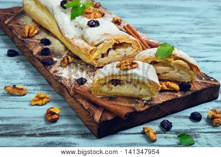 Cottage cheese and raisin cinnamon strudel with icing sugar ingredients for curd strudel raisins cinnamon sticks walnuts mint on cutting board blue wooden background