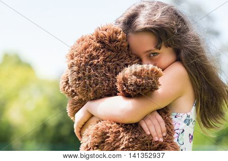Cute little girl embracing her new teddy bear and looking at camera. Portrait of lovely female child with her peluche outdoor. Little girl playing with her doll.