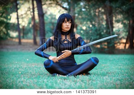 Beautiful girl sitting on the grass and holding samurai sword. Original cosplay character